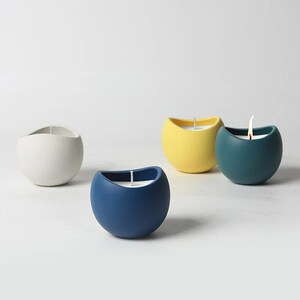 May include: Four round, ceramic candle holders in white, yellow, blue, and teal. Each holder has a single candle inside.
