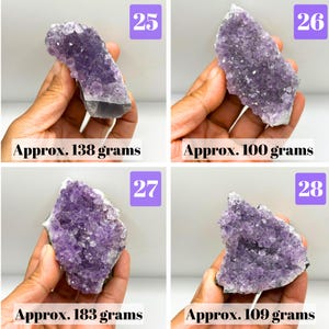 May include: Four amethyst crystal clusters labeled 25, 26, 27, and 28. The purple mineral specimens have jagged, crystalline surfaces. The weights are listed as approximately 138 grams, 100 grams, 183 grams, and 109 grams respectively.