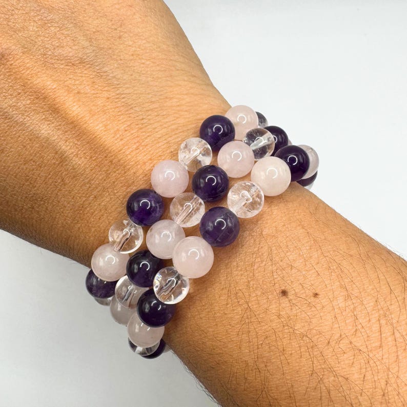 May include: A bracelet made with amethyst, rose quartz, and clear quartz beads. The bracelet is layered with three strands of beads.