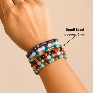 K&ouml;nnte beinhalten: Eine Sammlung von Armb&auml;ndern mit Perlen in verschiedenen Farben, darunter Gr&uuml;n, Rot und Lila. Die Perlen haben einen Durchmesser von ca. 6 mm. Die Armb&auml;nder sind an einem Handgelenk gestapelt.