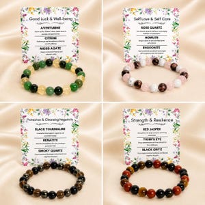 K&ouml;nnte beinhalten: Vier Edelstein-Perlenarmb&auml;nder mit Informationskarten. Die Armb&auml;nder sind gr&uuml;n, rosa, braun und rot. Die Karten haben florale R&auml;nder und Text &uuml;ber die Eigenschaften der Steine, darunter Aventurin, Rosenquarz, schwarzer Turmalin und roter Jaspis.