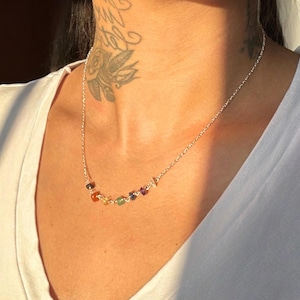 May include: A silver chain necklace with a row of colourful gemstones. The stones are in a rainbow order, starting with red and ending with purple.