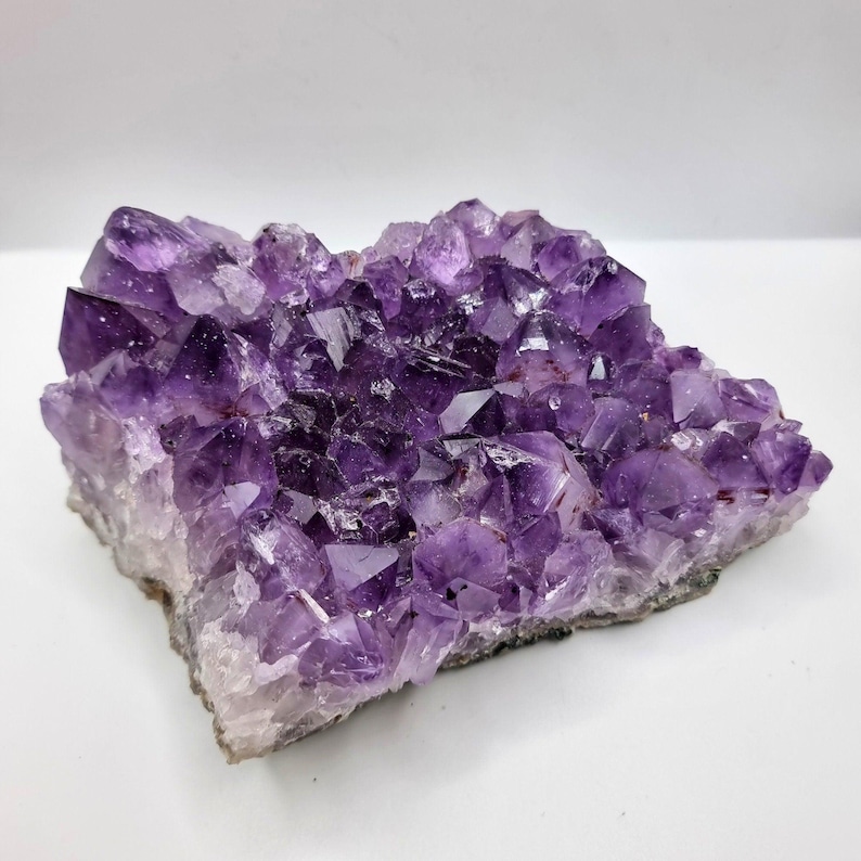 May include: A raw amethyst crystal cluster featuring numerous deep purple, pointed quartz points. The specimen displays a natural, jagged formation with varying shades of violet and translucent crystalline structures throughout the entire piece.