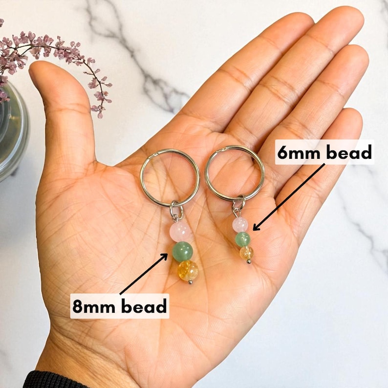 May include: Two keychains with silver rings, each featuring a cluster of colorful beads. One keychain has 8mm beads, the other has 6mm beads. The beads are pink, green, and yellow. The keychains are held in a hand.