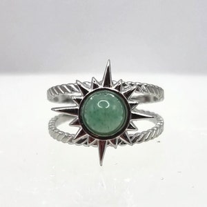 May include: A silver ring with a green stone set in a starburst design. The ring has a double band.