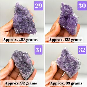 May include: Four amethyst crystal clusters labeled 29, 30, 31, and 32. The clusters weigh approximately 203 grams, 135 grams, 92 grams, and 83 grams respectively. Each piece features deep purple, jagged crystal points on a grey stone base.