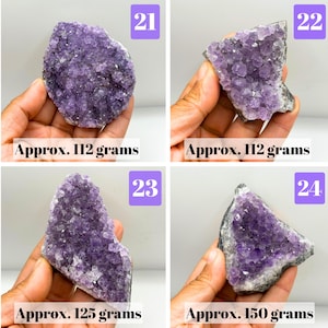 May include: Four purple amethyst crystal clusters labeled 21, 22, 23, and 24. Item 21 weighs 112 grams, item 22 weighs 112 grams, item 23 weighs 125 grams, and item 24 weighs 150 grams. Each piece features jagged, crystalline surfaces.