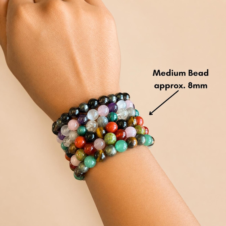 K&ouml;nnte beinhalten: Eine Sammlung von Armb&auml;ndern mit Perlen in verschiedenen Farben, darunter Schwarz, Lila, Rot, Gr&uuml;n und Gelb. Die Perlen sind etwa 8 mm gro&szlig;. Die Armb&auml;nder sind &uuml;bereinander gestapelt.