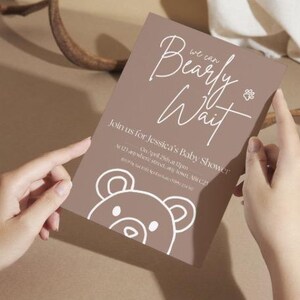 Puede incluir: Una invitaci&oacute;n marr&oacute;n para baby shower con el texto "Bearly Wait" en escritura blanca. La invitaci&oacute;n incluye detalles para el baby shower de Jessica, con una ilustraci&oacute;n de oso y una huella de pata.