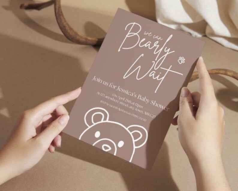 Puede incluir: Una invitaci&oacute;n marr&oacute;n para baby shower con el texto "Bearly Wait" en escritura blanca. La invitaci&oacute;n incluye detalles para el baby shower de Jessica, con una ilustraci&oacute;n de oso y una huella de pata.