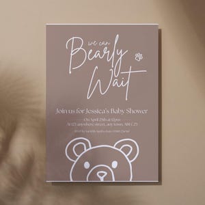 Puede incluir: Una invitaci&oacute;n de baby shower de color topo con texto blanco y una ilustraci&oacute;n de oso. La invitaci&oacute;n dice "Bearly Wait" e incluye detalles para el baby shower de Jessica, incluyendo la fecha, hora y lugar.