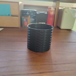 Może przedstawiać: Czarny, sześciokątny pojemnik na ołówki, wydrukowany w 3D, z geometrycznym wzorem.