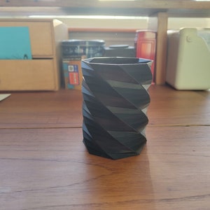 Può includere: Un portapenne nero, geometrico, stampato in 3D con un design a spirale.