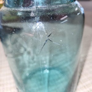 May include: A vintage blue glass jar with a metal lid and a crack in the glass.