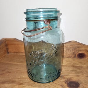May include: A vintage blue glass Ball jar with a wire bail closure. The jar has the text "Ball" and "Self Seal" printed on the front.