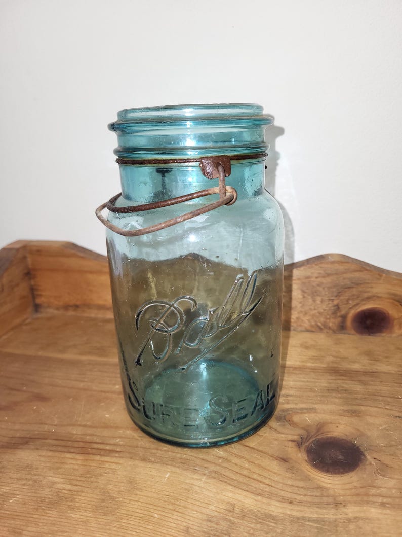 May include: A vintage blue glass Ball jar with a wire bail closure. The jar has the text "Ball" and "Self Seal" printed on the front.