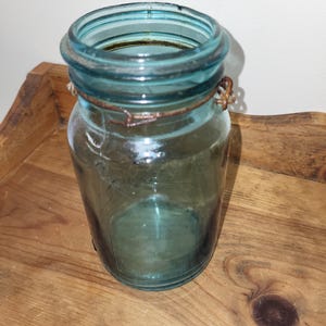 May include: A vintage blue glass jar with a wire bail closure. The jar is empty and has a slightly cloudy appearance.