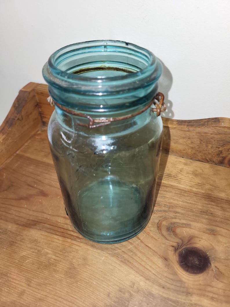 May include: A vintage blue glass jar with a wire bail closure. The jar is empty and has a slightly cloudy appearance.