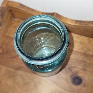 May include: A vintage blue glass jar with a metal lid and a wire bail closure. The jar is empty and has a slightly cloudy appearance.
