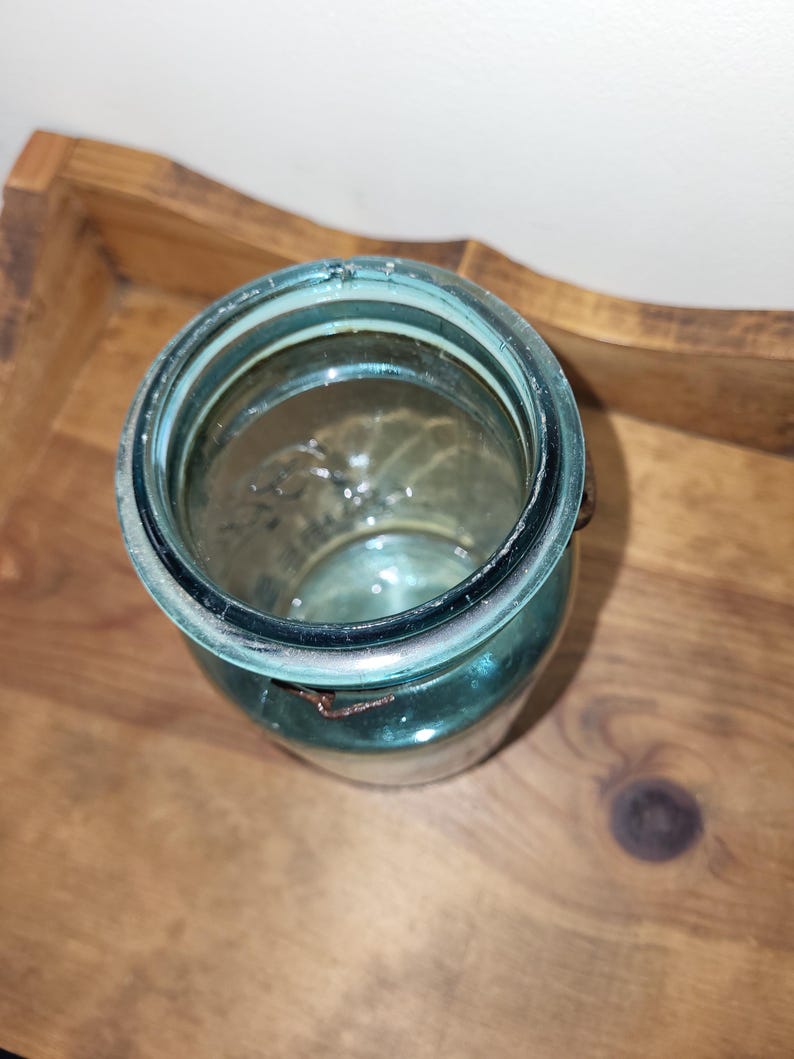 May include: A vintage blue glass jar with a metal lid and a wire bail closure. The jar is empty and has a slightly cloudy appearance.