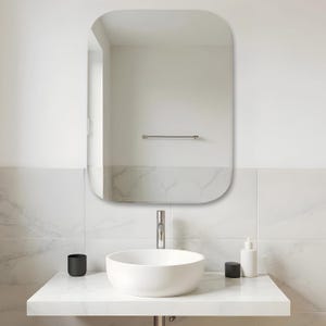 Könnte beinhalten: Ein rechteckiger Wandspiegel mit abgerundeten Ecken über einem weißen Aufsatzwaschbecken. Das Waschbecken verfügt über eine Chromarmatur und steht auf einer weißen Marmorplatte. Ein schwarzer Becher und ein weißer Seifenspender stehen daneben.
