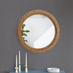 May include: A round mirror with a thick rope frame. The mirror is hanging on a grey wall.