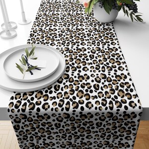 Peut inclure: Un chemin de table rectangulaire arborant un motif léopard répétitif dans des tons de noir, de beige et de blanc. Le tissu est posé à plat, mettant en valeur le design inspiré des animaux sur toute sa surface avec un imprimé dense.