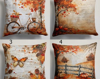 May include: A set of four square throw pillows featuring autumn-themed illustrations. Designs include a bicycle with a basket of apples, a tree with falling leaves, a butterfly on a script background, and a wooden fence with pumpkins and trees.
