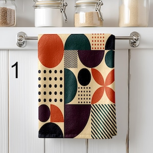 Puede incluir: Un paño de cocina con estampado geométrico con fondo beige. El diseño presenta círculos, semicírculos y cuadrados en tonos rojos, verdes, negros y morados. El paño está colgado de una barra plateada.