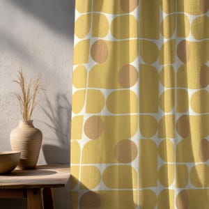 Op de afbeelding: Geel en wit gordijn met een retro design. Het gordijn heeft een herhalend patroon van afgeronde vormen in geel en perzik, omlijnd met witte lijnen. Het gordijn hangt voor een witte muur.