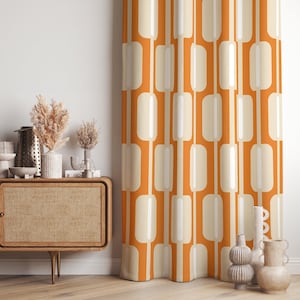 Può includere: Tenda a fantasia arancione e crema. Il motivo presenta rettangoli verticali color crema con centri bianchi su sfondo arancione. La tenda è appesa davanti a un muro bianco.