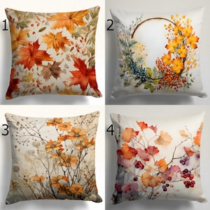Pode incluir: Quatro designs de almofada diferentes com ilustrações de aquarela de folhas de outono, flores e bagas. As almofadas são todas brancas com um fundo bege.