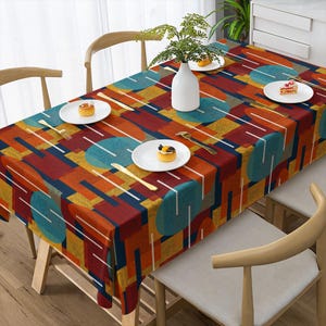 Könnte beinhalten: Eine rechteckige Tischdecke mit einem geometrischen Muster aus überlappenden türkisfarbenen Kreisen, orangefarbenen Rechtecken und dunkelblauen Blöcken. Das Design enthält durchgehend dünne weiße vertikale Linien. Die Decke liegt auf einem Esstisch.