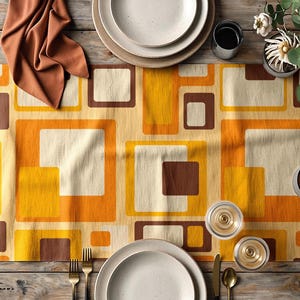 Könnte beinhalten: Ein rechteckiger Tischläufer mit einem sich wiederholenden geometrischen Muster aus überlappenden Quadraten und Rechtecken in Senfgelb, gebranntem Orange, Creme und Dunkelbraun, ausgelegt auf einer Holzoberfläche mit Tellern und Besteck.