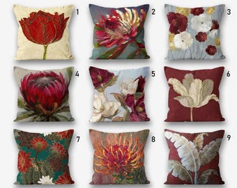 May include: Nine decorative throw pillows with floral designs. The pillows feature various flowers in shades of red, white, yellow, and green. The backgrounds vary in color, including teal, burgundy, and cream. The pillows are square-shaped and likely made of fabric.