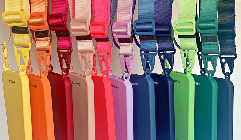 May include: A collection of colorful phone cases with matching lanyards. The cases are in shades of yellow, orange, red, pink, purple, blue, and green. Each case has a lanyard with a matching color. The cases have the word "NVPP" printed on them.