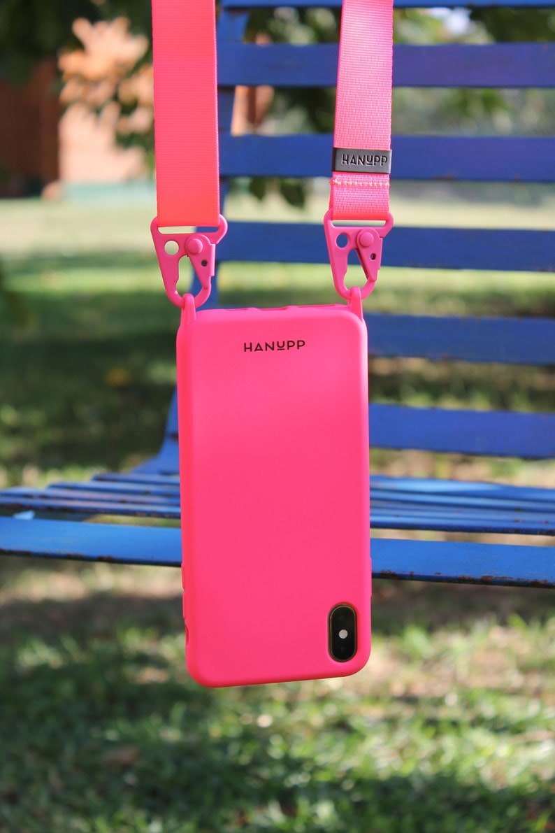 May include: Bright pink phone case with a matching strap, hanging against a blue bench. The case has the brand name "HANYPP" printed on it. The strap is attached with pink clips.