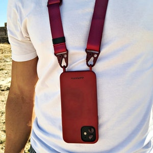 May include: A red phone case with the word "HANYPP" printed on it, attached to a burgundy lanyard. The lanyard has metal clips and is worn around the neck. The phone case has a dual-lens camera.
