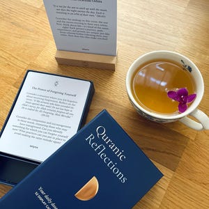 Puede incluir: Una caja azul con el texto "Reflexiones Cor&aacute;nicas" y un dise&ntilde;o de media luna dorada. La caja contiene 52 tarjetas de exhibici&oacute;n y un soporte de madera. El texto "Tu dosis diaria de serenidad espiritual." est&aacute; impreso en la caja.