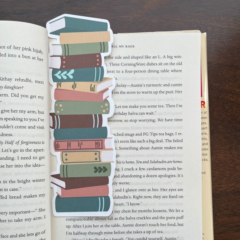 Peut inclure: Une pile de livres color&eacute;s avec un marque-page repr&eacute;sentant une pile de livres. Le marque-page est en papier et pr&eacute;sente un design fantaisiste. Le texte sur la page est "All My Rage".