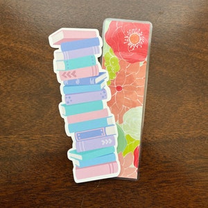 Peut inclure: Une pile de livres color&eacute;s avec un marque-page floral. Le marque-page a un motif floral rose, vert et jaune.