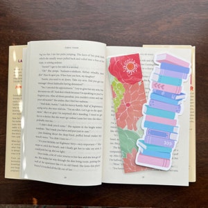 Peut inclure: Une pile de livres color&eacute;s avec un sch&eacute;ma de couleurs rose, bleu et violet. Les livres sont empil&eacute;s les uns sur les autres et ont un fond blanc. Le marque-page est une pile de livres avec un motif floral.