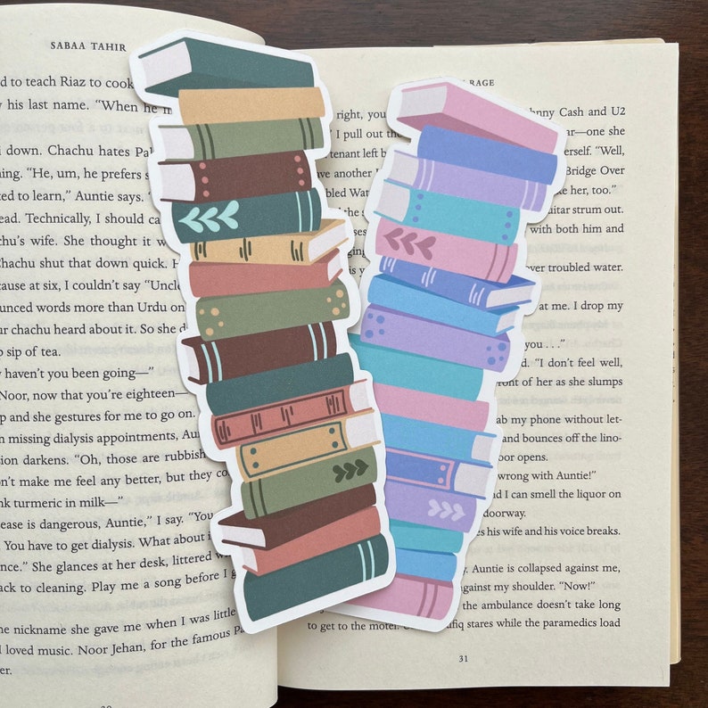 Peut inclure: Deux marque-pages empilables en forme de livre color&eacute;s. Le marque-page de gauche a une pile de 10 livres dans des tons de brun, vert et rose. Le marque-page de droite a une pile de 10 livres dans des tons de bleu, rose et violet.