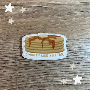 Könnte beinhalten: Ein weißer Aufkleber mit einer Cartoon-Illustration eines Stapels Pfannkuchen mit Sirup und einer Butterflocke obenauf. Der Text "SMOOTH LIKE BUTTER" ist unter den Pfannkuchen gedruckt.