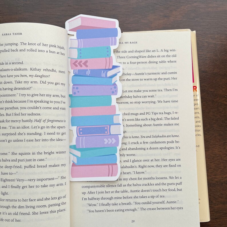 Peut inclure: Une pile de livres color&eacute;s avec un marque-page repr&eacute;sentant une pile de livres. Le marque-page est plac&eacute; dans un livre avec le texte "All My Rage".