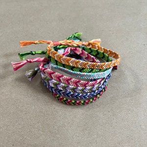 May include: A stack of colorful friendship bracelets with chevron patterns in shades of pink, green, orange, and blue.