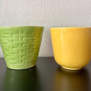 May include: Two ceramic planters are displayed side by side. The left planter is light green with a raised, woven basket-weave texture. The right planter is a smooth, solid yellow with a glossy finish and a rounded, tapered base shape.