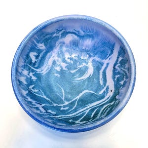 May include: A round ceramic bowl with a blue and white marbled design. The bowl's interior features shades of blue and white, creating a swirling, ocean-like pattern. The rim is a darker shade of blue.
