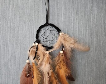 May include: A black dreamcatcher with brown and beige feathers hanging from it. The dreamcatcher is tied to a black ribbon.