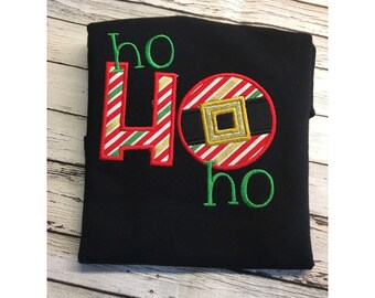May include: Black t-shirt with a red, white and green embroidered "Ho Ho" design. The "O" is a circle with a red and white striped pattern and a black belt with a gold buckle.